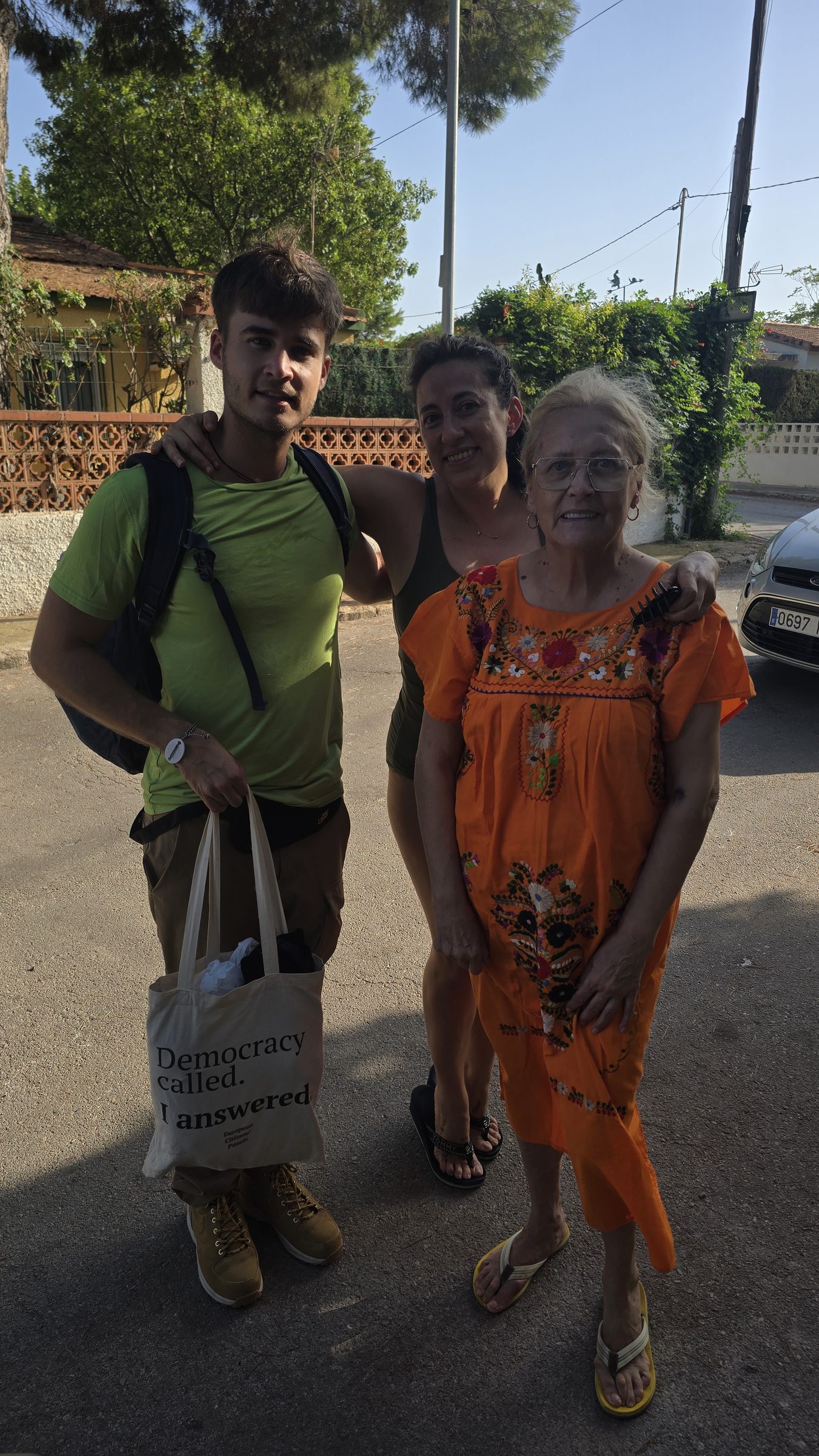 Tres personas en una calle soleada; una lleva una bolsa de tela con el lema «Democracy called. I answered.»