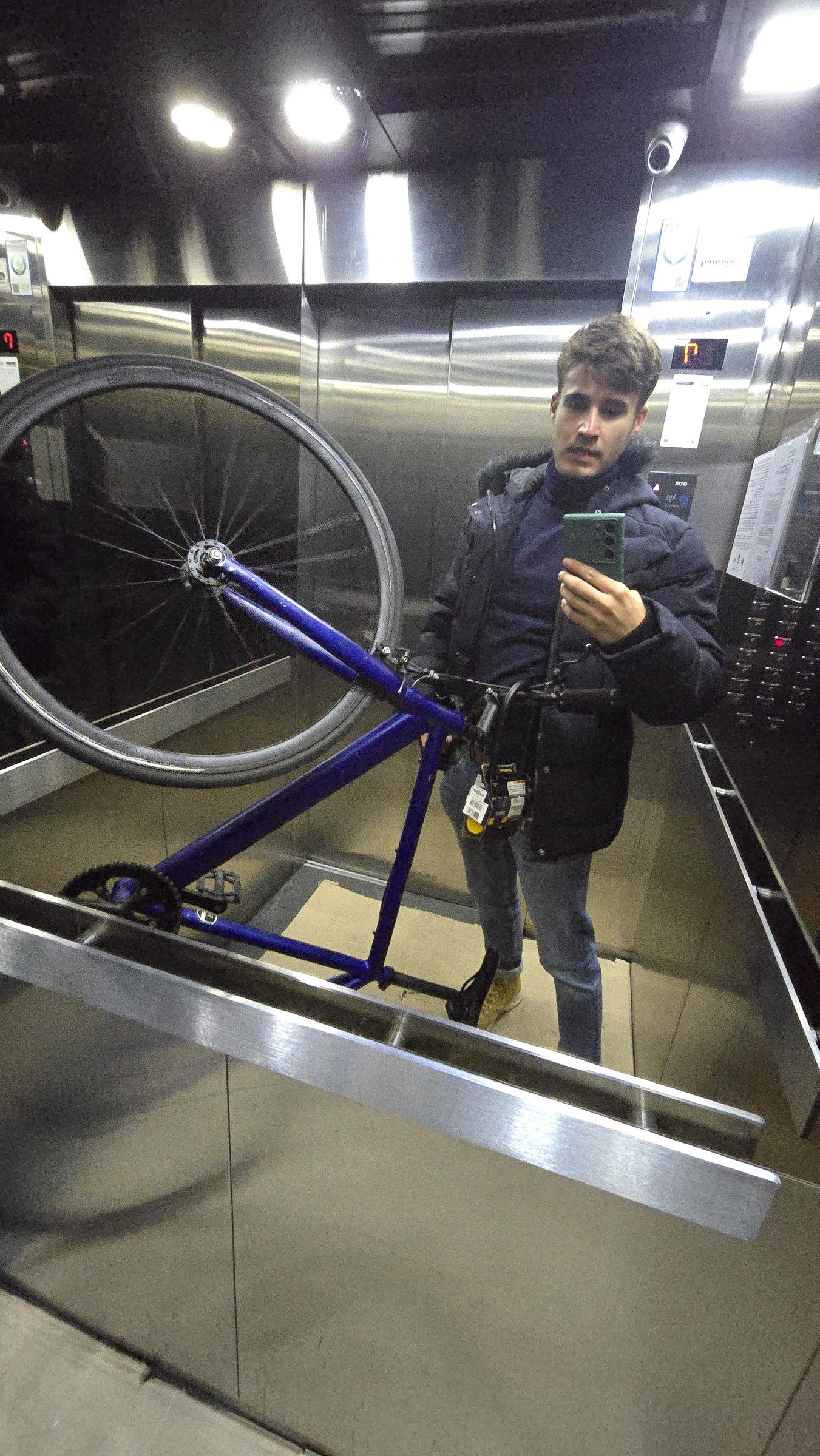 Selfie en el espejo de un ascensor, con la bicicleta azul apoyada al lado