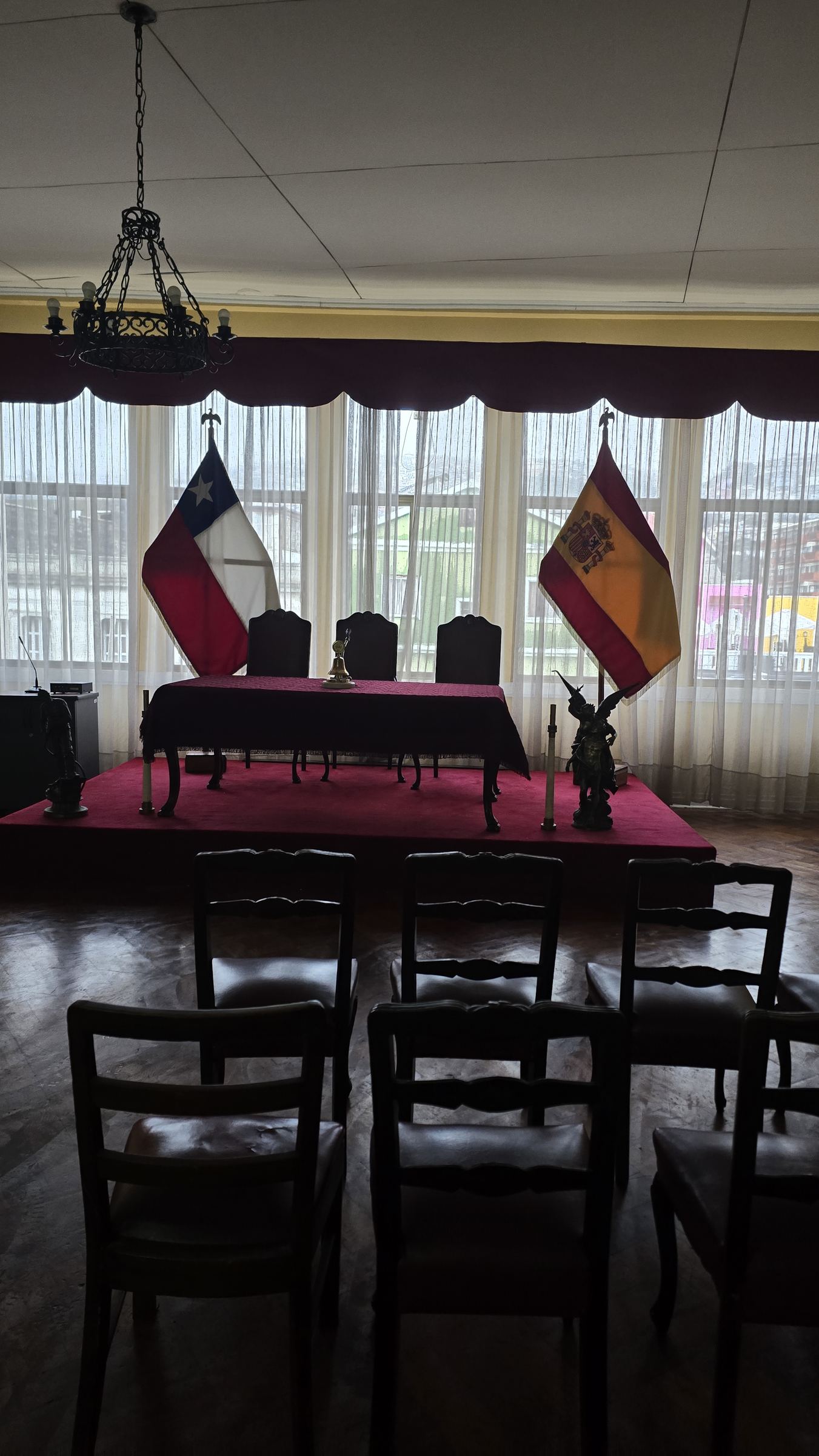 Una sala con las banderas de Chile y España junto a una tarima con sillas