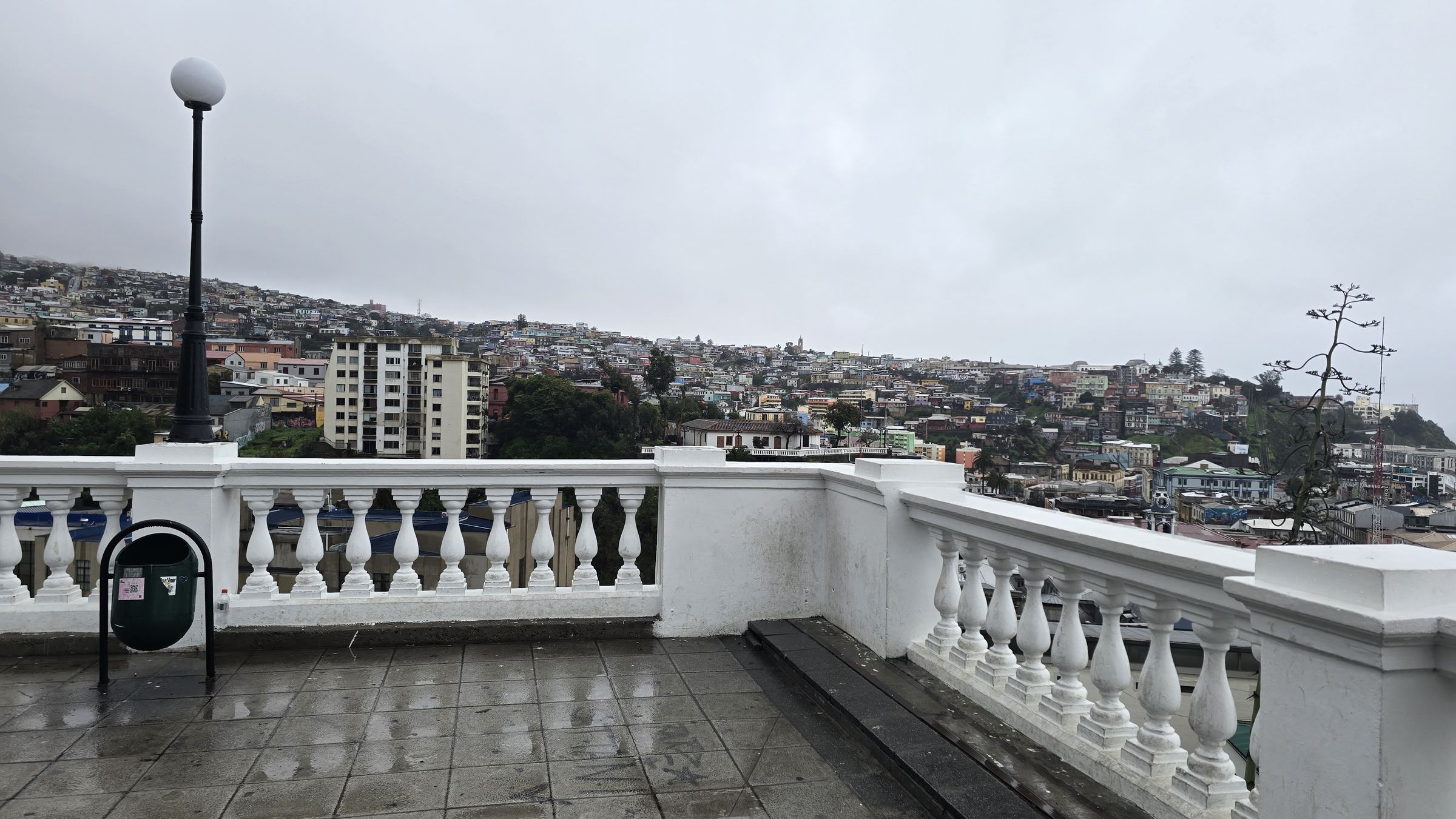 Una terraza con balaustrada blanca y vistas a los cerros de Valparaíso en un día lluvioso