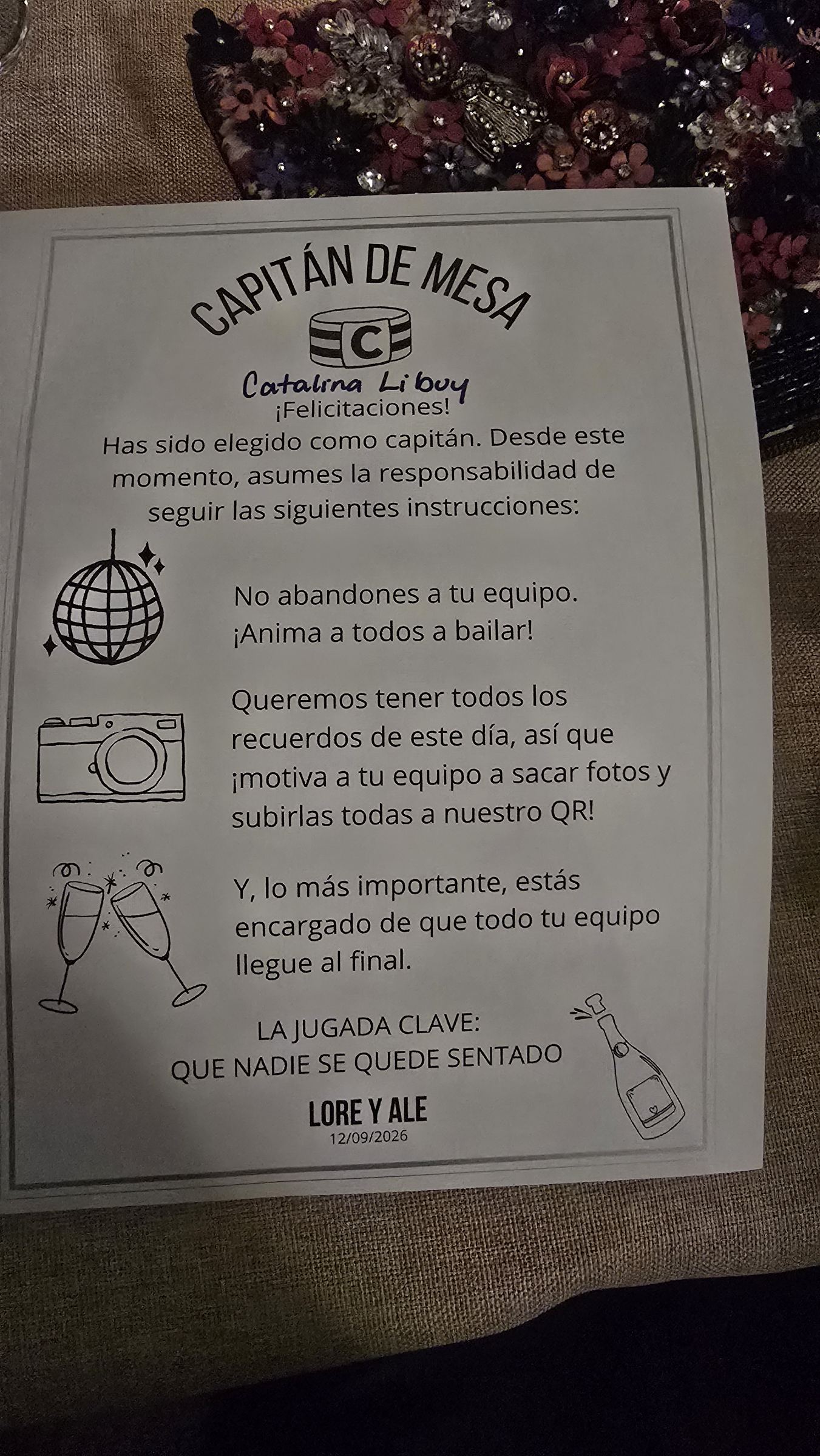 Una tarjeta de mesa con instrucciones y el nombre de los novios, con globos y una bola de discoteca dibujados alrededor