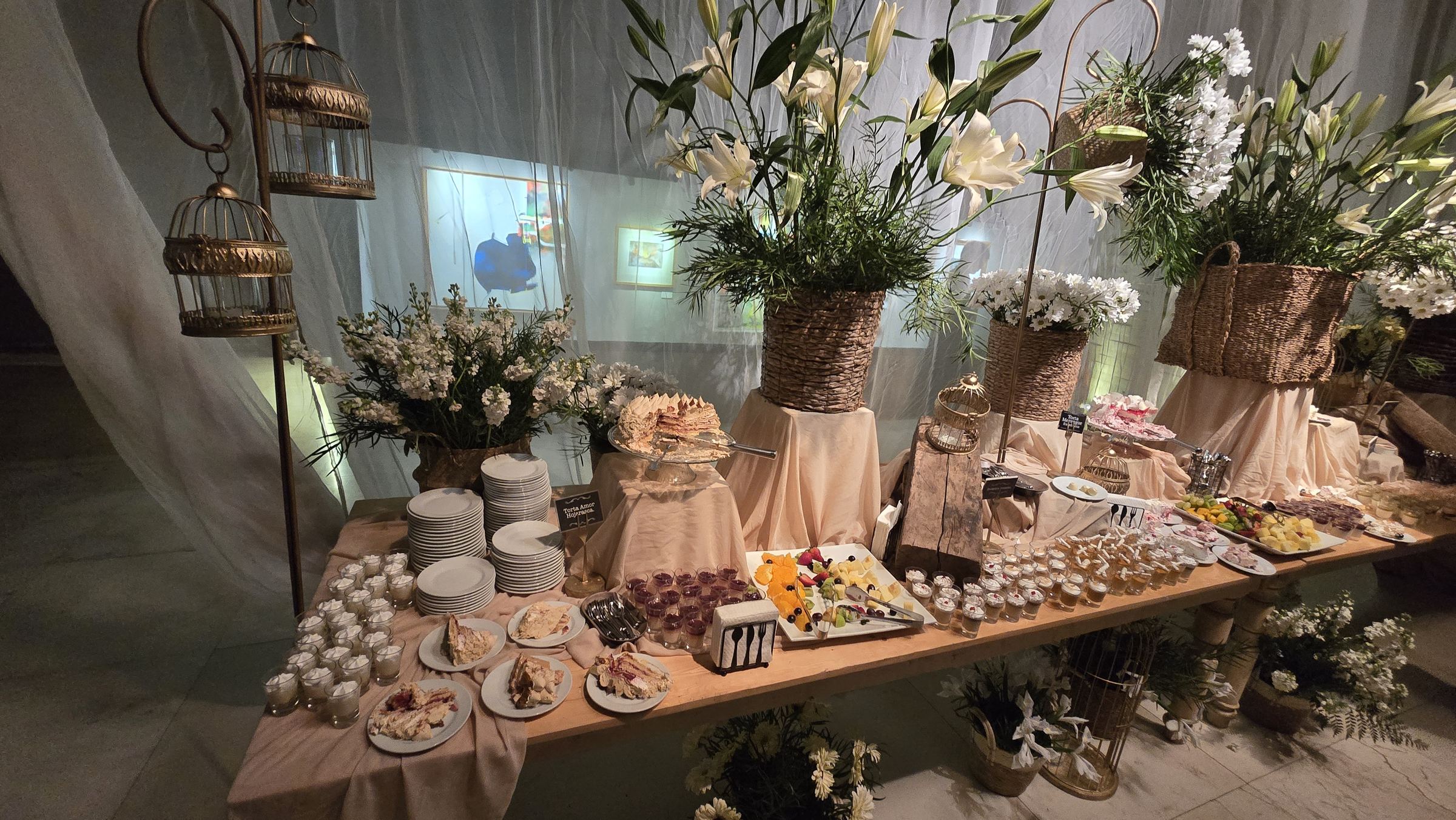 Una mesa de postres decorada con flores y jaulas doradas, en la fiesta de una boda